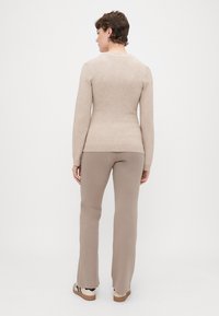 Bežs adījuma krekls ar garām piedurknēm un apaļu izgriezumu, saskaņots ar bežām platām biksēm. Gluda tekst�ūra un vienkāršs dizains.