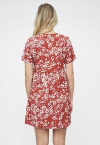 Punainen kukkakuosinen mekko, jossa on lyhyet hihat ja levenevä vyötärö, pyöreä pääntie ja liehuva helma. Kangas vaikuttaa kevyeltä.