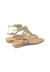 Sandalias planas beige con diseño de tiras tipo thong, decoradas con acentos de gemas en tonos verde y azul, detalle de cadena dorada y un sutil tacón cuadrado.