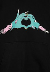 Fekete kapucnis pulóver, amelynek grafikája két kezét szívformába összekulcsoló kéz. A kezek türkiz színűek, rózsaszín részletekkel és látható ujjak.