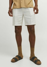 Shorts en lin blancs, de longueur courte, associés à des chaussettes marron jusqu'aux genoux et des sandales bicolores avec des brides noires et des boucles.