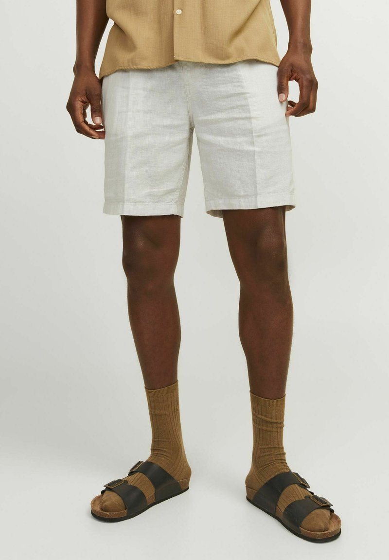 Shorts en lin blancs, de longueur courte, associés à des chaussettes marron jusqu'aux genoux et des sandales bicolores avec des brides noires et des boucles.