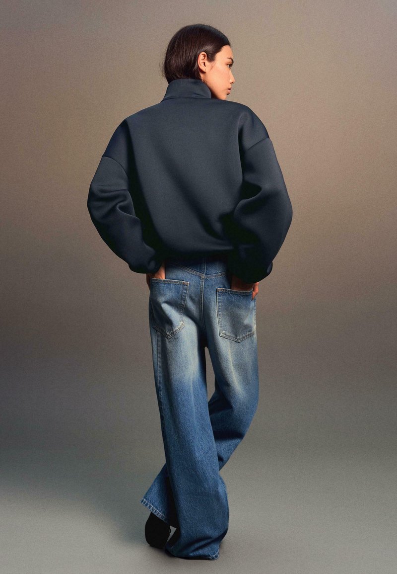 Overmaatse donkergrijze sweatshirt met hoge kraag, gecombineerd met lichtblauwe wijde denim jeans met achterzakken en een vervaagde afwerking.
