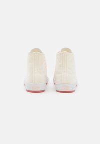 Bílé plátěné vysoké tenisky s růžovou gumovou podrážkou, s kulatým logem na zadní straně a vertikálním stehem.