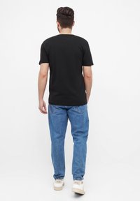 Zwarte katoenen T-shirt met korte mouwen, gecombineerd met blauwe spijkerbroek. Model draagt witte sneakers met logo op de hak. Eenvoudig ontwerp, geen patronen.
