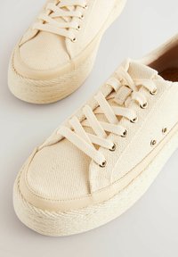 Baskets en toile beige avec bout rond, surface texturée et semelle intermédiaire en jute tressé. Comprend des œillets dorés et des lacets en coton assortis.