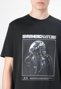 Black t-shirt featuring a graphic of a jellyfish with mechanical tentacles, the text "SYNTHETIC NATURE" above, and an Oakley logo below.