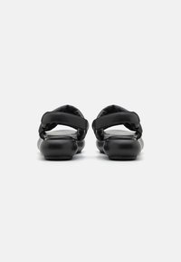 Black sandals featuring rounded soles, padded fabric straps, and a smooth exterior. Minimalist design with no visible hardware.