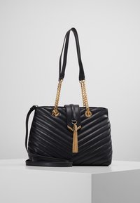 Mustat tikatut käsilaukut, joissa on kultaketju korostuksia, koristeellinen tupsu ja kaksoishihnat. Ominaisuudet sisältävät rakenteellisen muodon ja sileän tekstuurin.