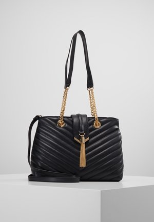 Sort quiltet håndtaske med guld kæde detaljer, en dekorativ frynse og dobbelte remme. Har en struktureret form og glat tekstur.