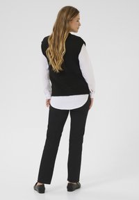 Black knitted vest over a white shirt, paired with black pants. Smooth texture; fitted design. The outfit features a casual, layered look.