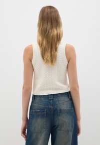 Top in maglia color crema con motivo a treccia, abbinato a jeans in denim blu a vita alta con due tasche posteriori e leggeri segni di usura.