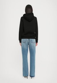 Un hoodie noir avec une poche kangourou, associé à un jean large bleu clair. La tenue présente une coupe décontractée et confortable.