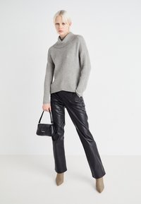 Grijze geribbelde trui met een hoge kraag, gecombineerd met zwarte leren broeken. Model houdt een kleine zwarte handtas vast. Schoenen in neutrale tinten met een puntige neus.