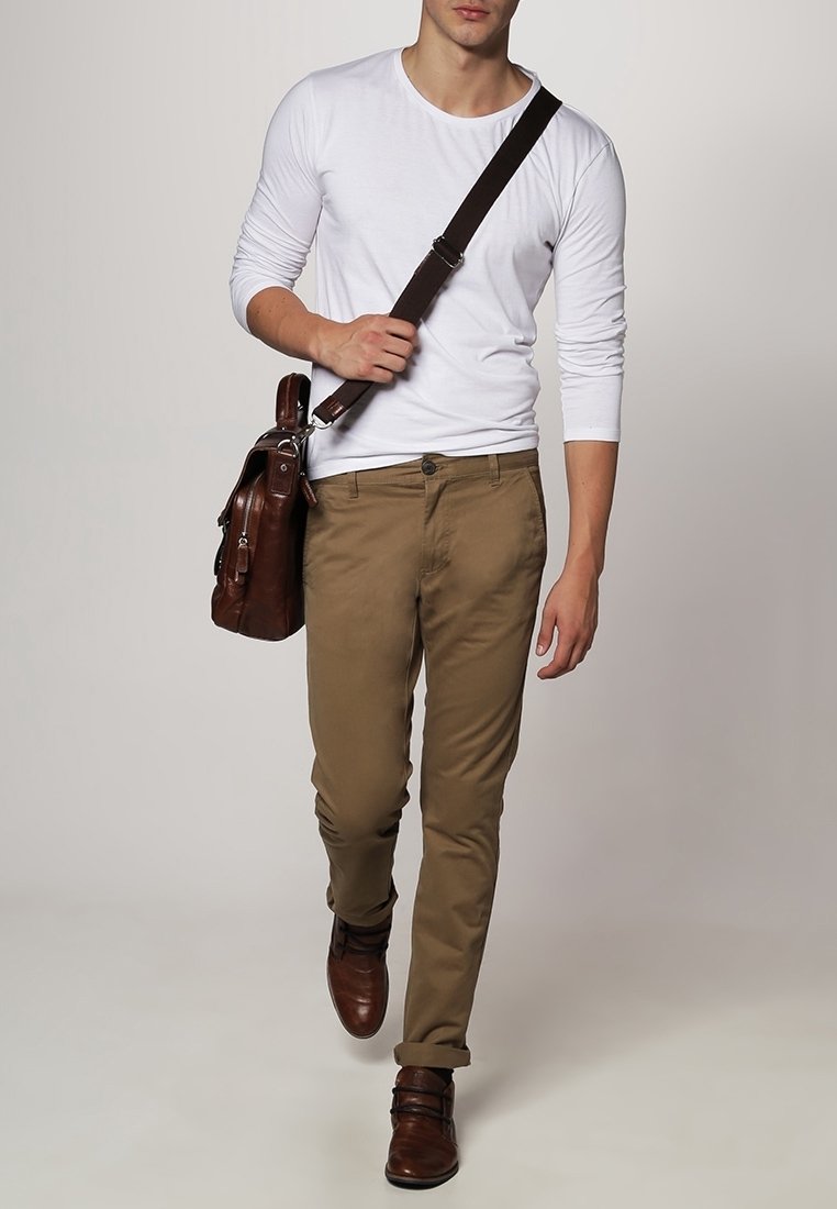 Homme marchant portant une chemise blanche à manches longues, un pantalon kaki, des chaussures en cuir marron, et portant un sac à bandoulière en cuir marron.