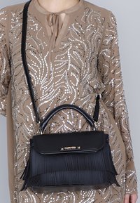 Borsa a mano in pelle nera con frange, forma strutturata, manico superiore e tracolla regolabile. Accenti di hardware dorato notevoli sulla parte anteriore.