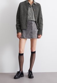Grijze gebreide cardigan met een geribbelde textuur, knoopsluiting, gestreept shirt, denim minirok, zwarte kniekousen en zwarte schoenen.