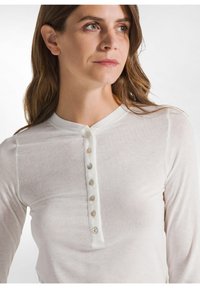 Maglietta henley a maniche lunghe bianca realizzata in tessuto leggero e testurizzato, con scollatura arrotondata e sette bottoni decorativi sul davanti.