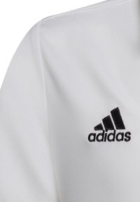 Weißes Sportshirt aus einem glatten Stoff, mit einem schwarzen Adidas-Logo und drei Streifen. Das Design ist schlicht und minimalistisch.