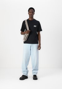 Black short-sleeve t-shirt with white text, light blue baggy jeans, gray crossbody bag, and black athletic shoes. Clean and modern look.