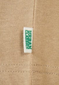 Țesătură bej cu o textură fină de tricot. Prezintă o etichetă albă cu textul verde "URBAN CLASSICS" coaptă în cusătură.
