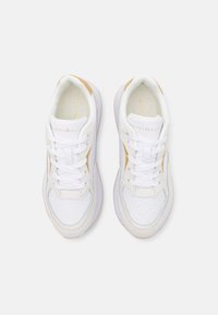 Białe sneakersy z jasnobrązowymi akcentami, posiadające teksturowaną powierzchnię, płaskie sznurówki i amortyzowaną podeszwę. Logo wydrukowane na języku.