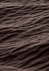 Tissu brun froissé avec des plis diagonaux irréguliers créant une surface texturée sous un éclairage doux.