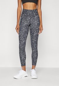 Sötét szürke, magas derekú leggings absztrakt, texturált kamuflázs mintával, fehér sportcipővel párosítva.