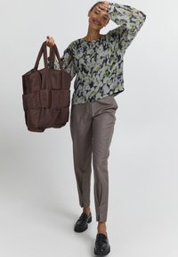 Blusa trasparente a fantasia floreale verde e viola; borsa a tracolla imbottita marrone; pantaloni grigi su misura; mocassini neri con suola spessa.