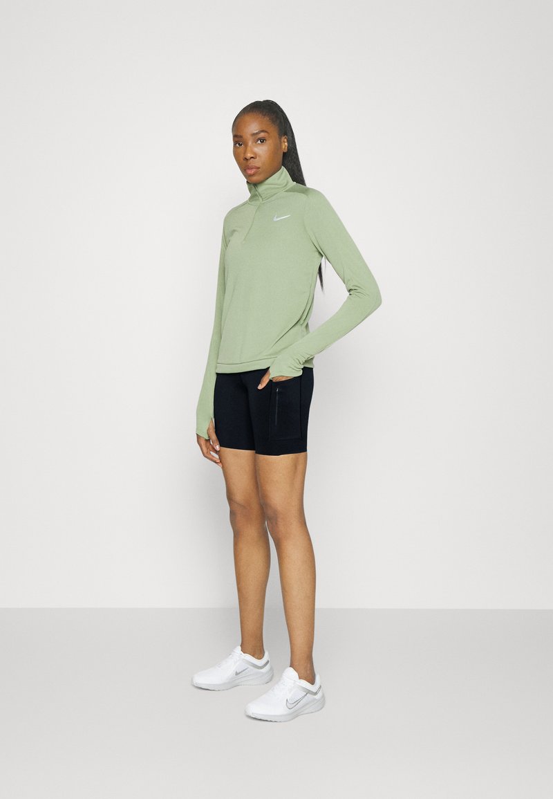 Sudadera de cremallera de manga larga verde claro, pantalones cortos negros y zapatillas blancas. Diseño ajustado con el logo de Nike en la parte superior, textura suave, estilo atlético.