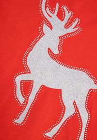 Czerwona tkanina z srebrnym brokatowym wzorem renifera, obrysowanym małymi cyrkoniami, podkreślającymi kształt postaci i rogi.