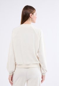 Felpa di colore crema chiaro con scollatura arrotondata, maniche raglan e polsini a coste. Materiale morbido e peloso con una vestibilità rilassata.