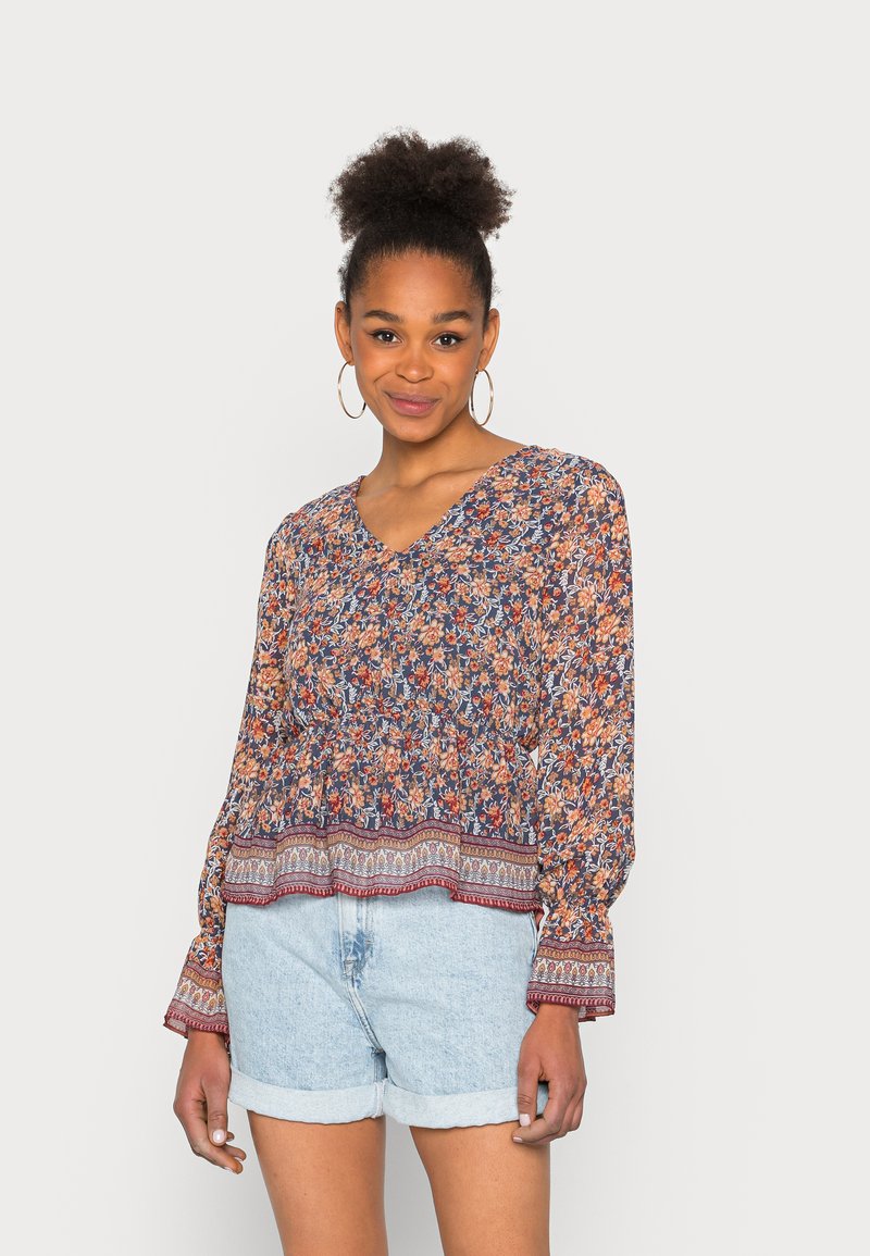 Blusa floral com decote em V, mangas longas e cintura elástica em azul marinho, laranja e creme. Apresenta uma bainha estampada e tecido leve.