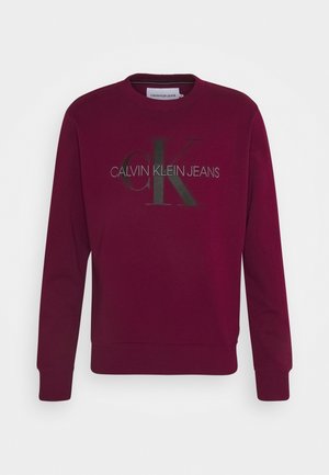 Bordeaux-colorettinen crewneck-collegepaita, joka on valmistettu puuvillasekoitteesta. Siinä on rohkea musta "CK" -logo ja "CALVIN KLEIN JEANS" -teksti metallinhohtoisessa hopeassa.