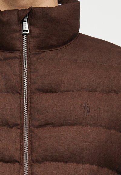 Καφέ μπουφάν με καπιτονέ ύφασμα, ψηλό γιακά, ασημένιο φερμουάρ και διακριτικό ραμμένο λογότυπο παίκτη πόλο στο αριστερό στήθος.