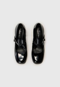 Black patent leather Mary Jane shoes with a rounded toe, ankle strap, and medium block heel. Smooth texture with minimal hardware.