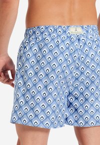Costume da bagno da uomo in azzurro chiaro con un motivo geometrico di quadrati e gocce. Presenta una vita elastica e un'etichetta sul retro.