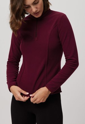 Sudadera de forro polar color marrón con un cuello alto y una cremallera corta. Presenta mangas largas y costuras laterales para un ajuste ceñido. Textura suave.
