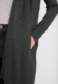 Dunkelgraue Strickjacke aus weichem Material, mit einem fallenden Vorderteil, gerippten Bündchen und einer sichtbaren seitlichen Tasche.