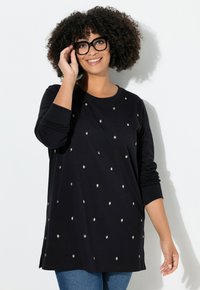 Maglietta nera a maniche lunghe con decorazioni di pois argentati, vestibilità morbida, colletto rotondo e polsini a coste, abbinata a jeans blu.