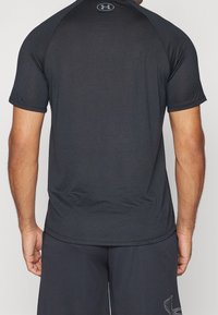 Svart atletisk t-shirt med korta ärmar, slät tyg, rundad halsringning och en logotyp på övre ryggen. Bärs med matchande mörka shorts.