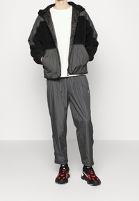 Sort og grå lynlåsjakke med struktureret fleece og ternet stof, parret med matchende ternede bukser og sneakers med røde accenter.