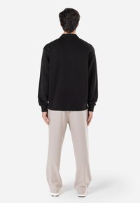 Sort sweatshirt med en afslappet pasform, ribbede manchetter og en stående krave, parret med lysebeige bukser med bred ben. Blød stofstruktur.