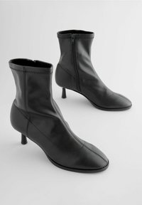 Bottes noires en cuir à hauteur de cheville avec un design ajusté, bout pointu et talons bas. Présente des zips latéraux et des coutures détaillées le long des seams.
