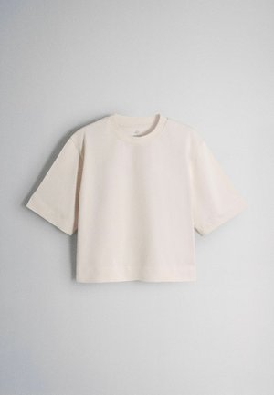 Beżowy krótki t-shirt z krótkim rękawem i okrągłym dekoltem na jasnoszarym tle.