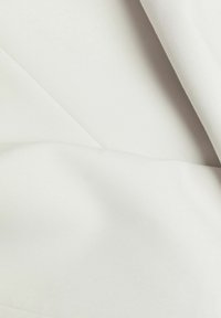 Närbild av vitt tyg med subtila diagonala veck och en slät, något texturerad yta.