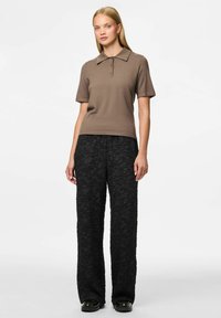 Bruine polo met kraag en korte mouwen, gecombineerd met zwarte textuur brede broek. Eenvoudige knopen op de polo. Glanzende zwarte schoenen.