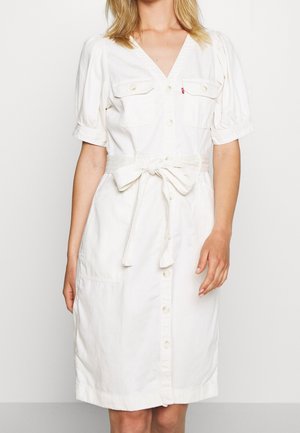 Robe blanche à manches courtes avec décolleté en V, boutonnage à l'avant, deux poches poitrine et une ceinture à la taille, fabriquée dans un tissu doux et texturé.