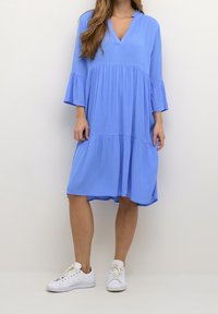 Robe bleu en A avec des manches cloche trois-quarts et un décolleté en V, faite d'un tissu léger ; associée à des baskets blanches.
