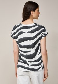 Schwarzes und weißes T-Shirt mit kurzen Ärmeln, das ein Zebra-Streifenmuster aufweist, lockere Passform und einen weichen Stoff hat.